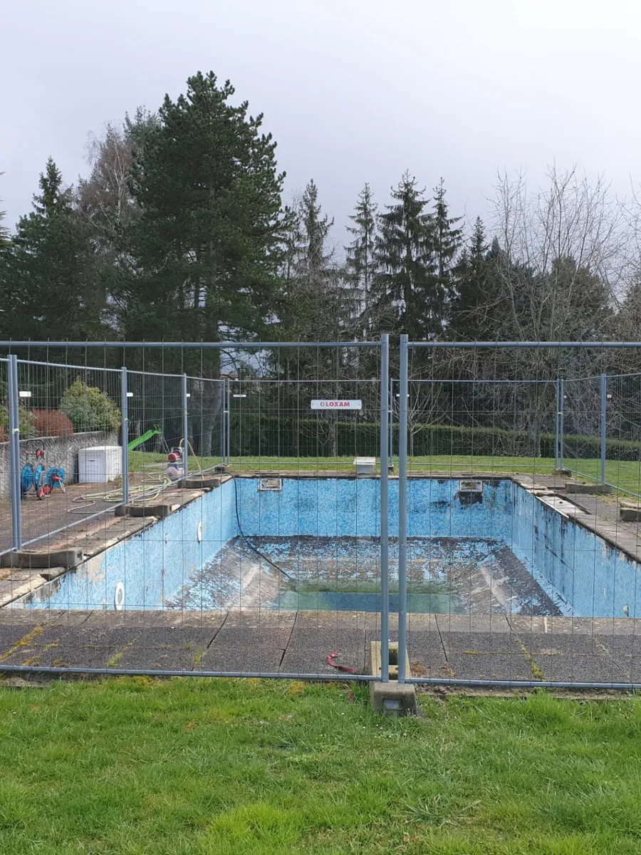 Avant : piscine vide en cours de rénovation, entourée d'une clôture de chantier